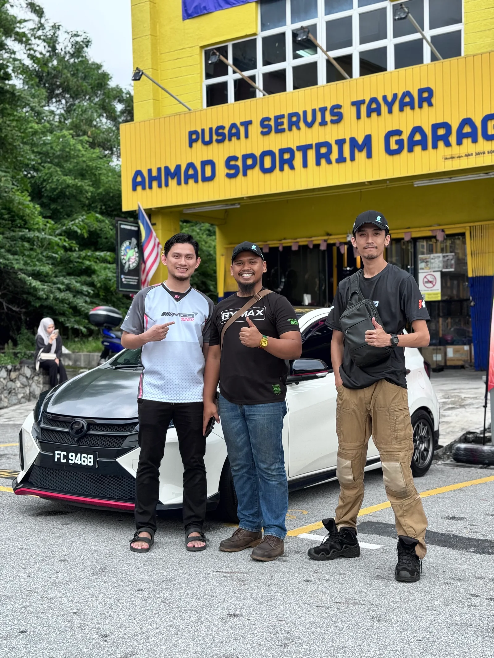 Three ASG community members beside a white Perodua outside the ASG workshop