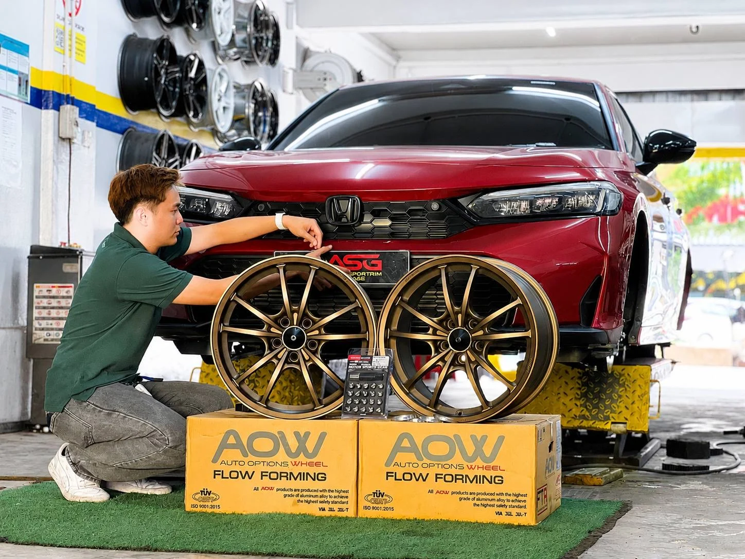 ASG team member presenting bronze sport rims in front of a red Honda