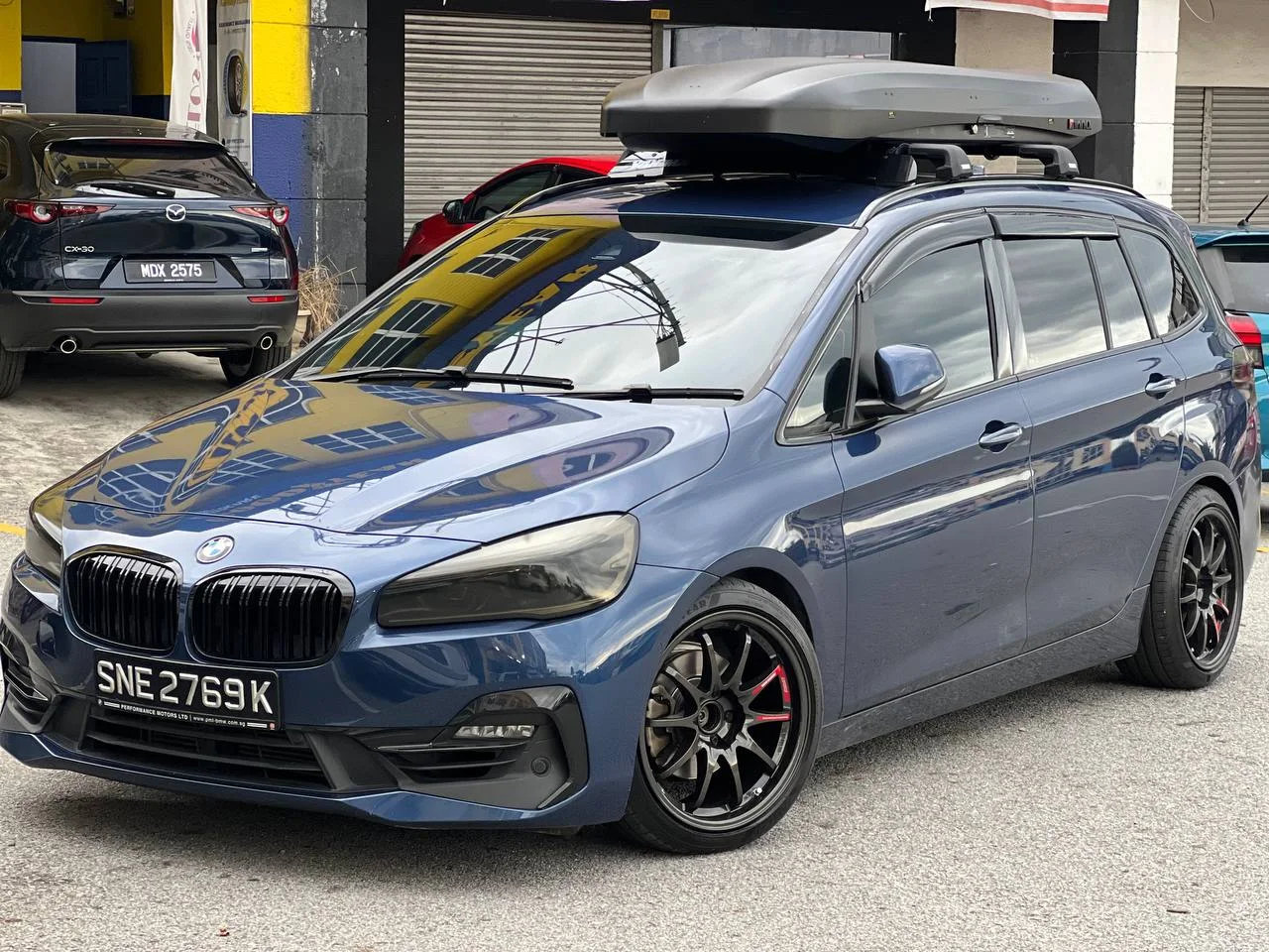 Blue BMW 2 Series Gran Tourer with aftermarket wheels and a roof box