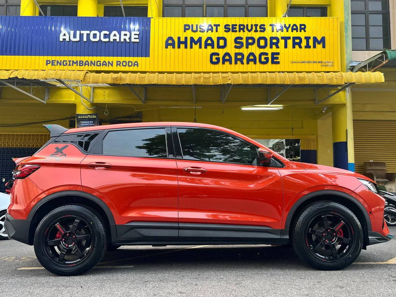 Red Proton SUV side profile with black five-spoke wheels outside ASG