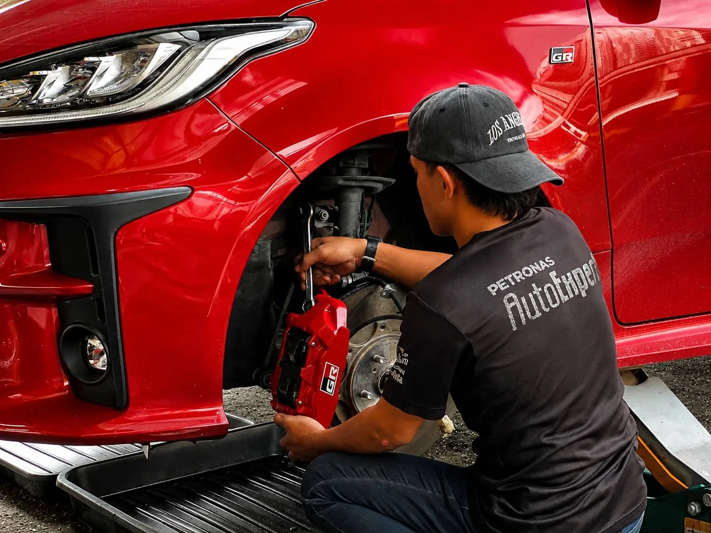 Technician working on the exposed brake assembly of a red car